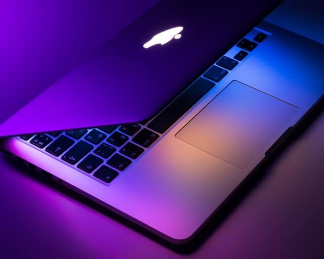 macbook laptop half closed with neon purple lights background